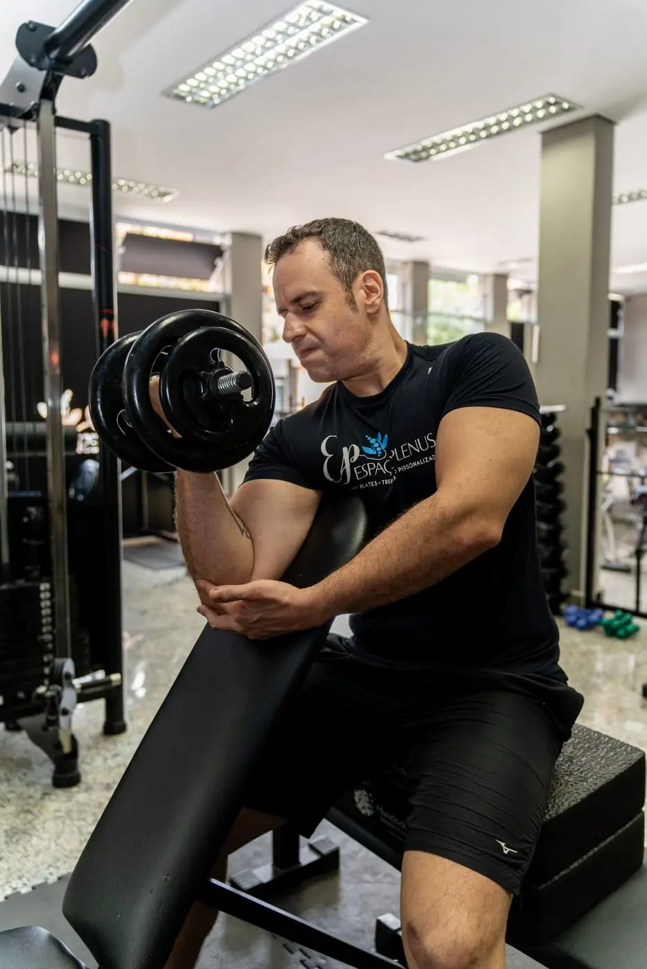 Personal trainer do Espaço Plenus demonstrando execução de exercício com halteres